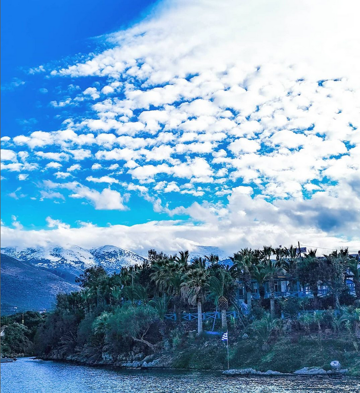 Paesaggio invernale a Creta con palme in riva al mare e montagne innevate sullo sfondo.